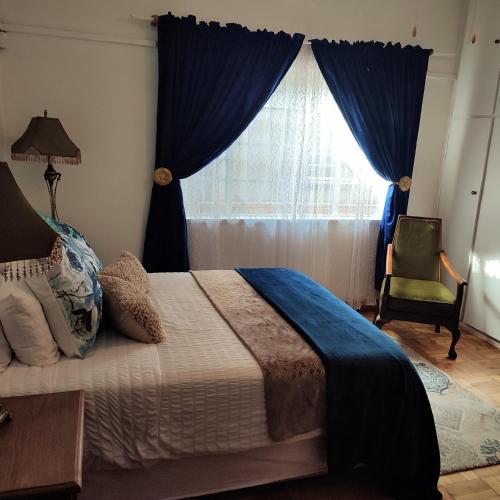 a bedroom with a bed with blue curtains and a window at Rehati Guesthouse in Potchefstroom