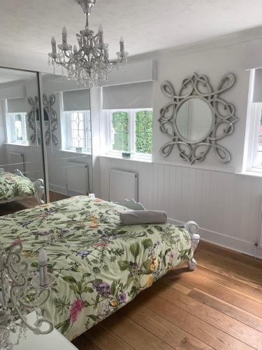 1 dormitorio con cama, espejo y lámpara de araña en Wychwood A Beautiful Country Style Bungalow, en Ash