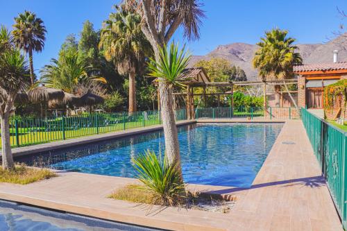 a swimming pool with palm trees and a fence at Hotel Naturaleza Vertientes de Elqui in El Molle