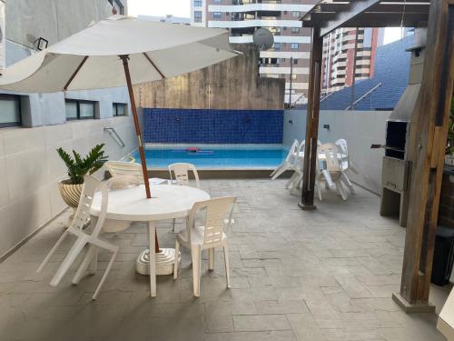 uma mesa branca e cadeiras com um guarda-sol num telhado em Confortável Apto com Manobrista Wi-fi - Tv Smart - piscina - Apto 703 em Maceió