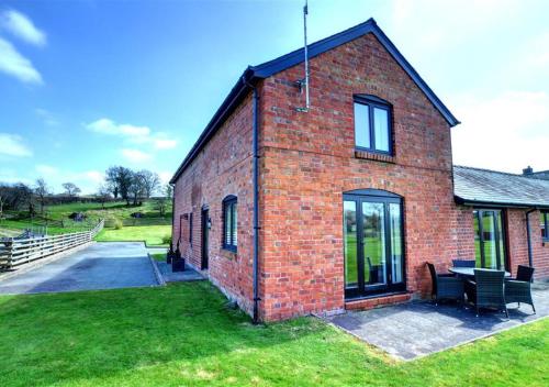 a red brick building with a bench on the grass at Y Beudy in Llandinam