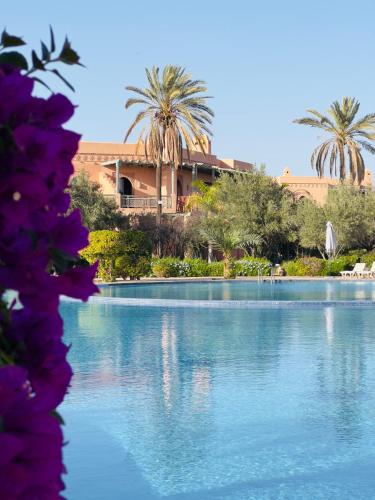 a swimming pool with palm trees and purple flowers at Palmeraie 3 Vue Piscine et Jardin in Marrakech
