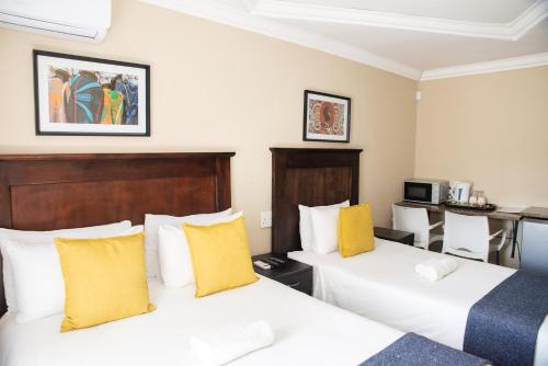 two beds in a hotel room with yellow pillows at M n M Guesthouse In Turfloop Mankweng in Polokwane