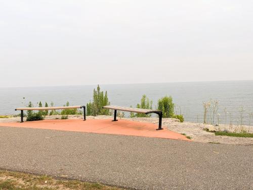 two benches sitting on a sidewalk near the water at PARADISE VILLa Bowmanville in Bowmanville