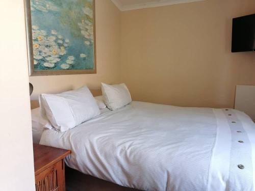 1 dormitorio con 1 cama blanca y una pintura en la pared en Redberry Guest House, en Mbabane