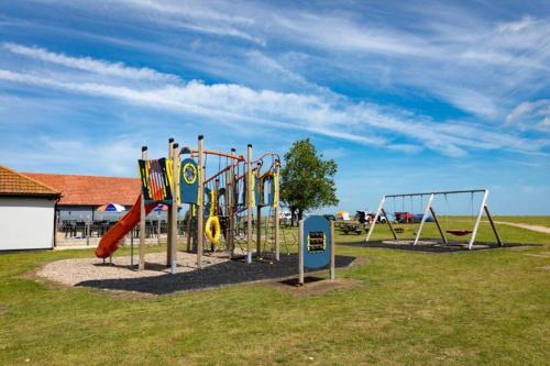 a playground with a bunch of swings in a field at Platinum Holiday Home by the Sea in Whitstable