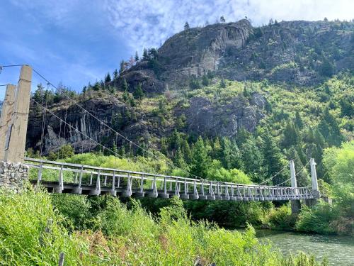 un puente colgante sobre un río frente a una montaña en Hostería de Montaña Las Pataguas en El Hoyo