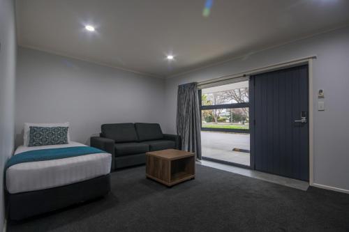 1 dormitorio con cama, sofá y puerta corredera de cristal en Antonio Mews Motel, en Stratford