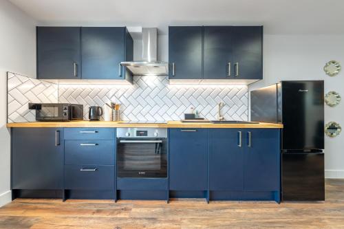 a kitchen with blue cabinets and a black refrigerator at 5 - West London Brand New Loft in London