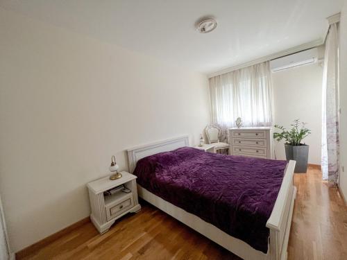 a white bedroom with a purple bed and a window at Oscar in Podgorica