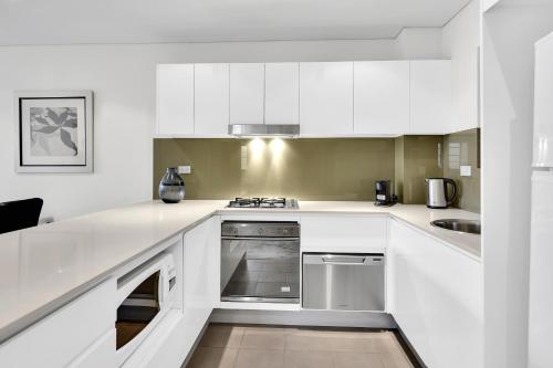 La cuisine est équipée de placards blancs et d'un four avec plaques de cuisson. dans l'établissement Spacious Two bedroom apartment - St Leonards AL25, à Sydney