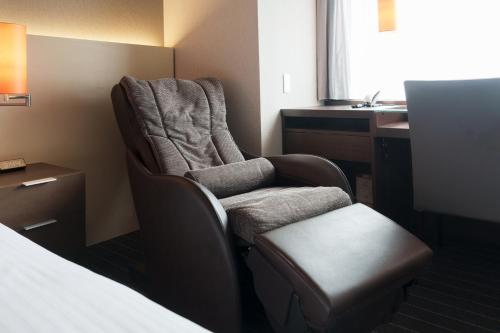 a room with a chair and a desk and a bed at Hotel Forza Oita in Oita