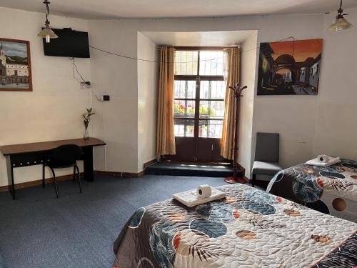 a room with two beds and a desk and a window at Hostal Benalcazar in Quito