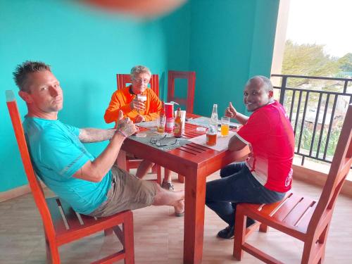 a group of three men sitting around a wooden table at Kiteme Comfort Lodge in Arusha