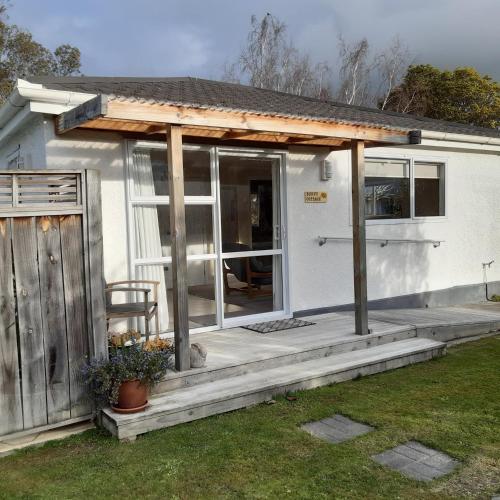 a small white house with a porch and a door at Bunny Cottage in Masterton