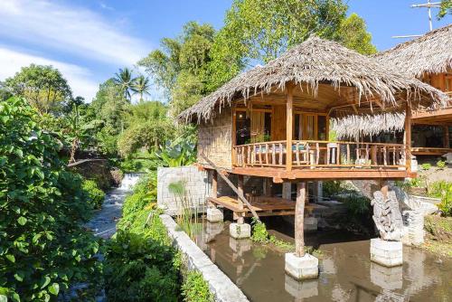 a house with a thatched roof and a river at Onong's Homestay & Cafe in Tomohon