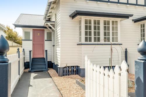 una casa bianca con una porta rossa e una recinzione di Cherry Tree Cottage! CBD Magic! a Toowoomba