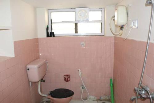 une salle de bains carrelée de rose avec des toilettes et une fenêtre. dans l'établissement The Ghosh's Home stay, à Hyderabad