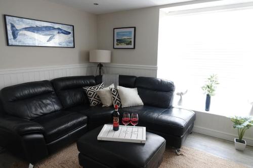 a living room with a black leather couch and two glasses of wine at 3 Bedroom Cottage in Conwy with Parking Sleeps 4 in Conwy