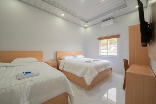 a white bedroom with two beds and a window at Lombokhouse Mandalika in Kuta Lombok