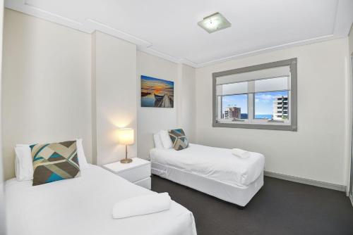 a white room with two beds and a window at Sandy Cove Apartment The Entrance 24 in The Entrance