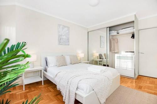 a white bedroom with a white bed and a plant at Perfect Manly Retreat. in Sydney
