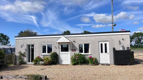 a small grey building with white doors and flowers at Runway Cottage in Coningsby