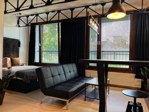ein Wohnzimmer mit einem schwarzen Ledersofa und einem Bett in der Unterkunft Loft Apartment Browary Warszawskie in Warschau