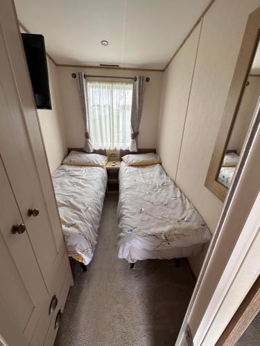 a small room with two beds and a window at Waterside mini lodge - pet friendly, WiFi, direct beach access & club on site - Meadow Lakes Caravan & Lodge Hire in Ingoldmells