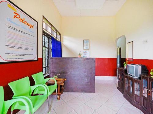 una sala de espera con sillas verdes y TV en Wisma Pelangi Palopo RedPartner, en Palopo