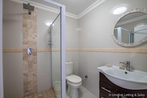 a bathroom with a toilet and a sink and a mirror at Cozumel 218 in Umdloti
