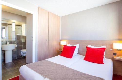 um quarto de hotel com uma cama com duas almofadas vermelhas em SOWELL HOTELS Le Pas du Loup em Isola 2000