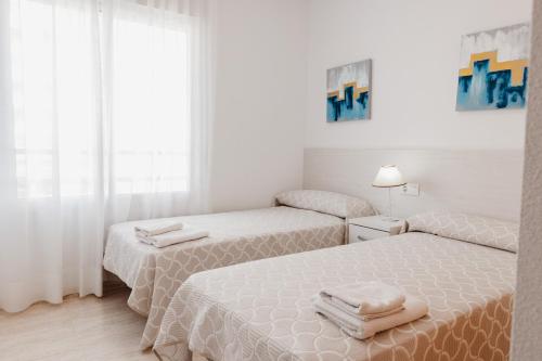 2 camas en una habitación blanca con cortinas blancas en Apartamentos Vistamar, en La Manga del Mar Menor