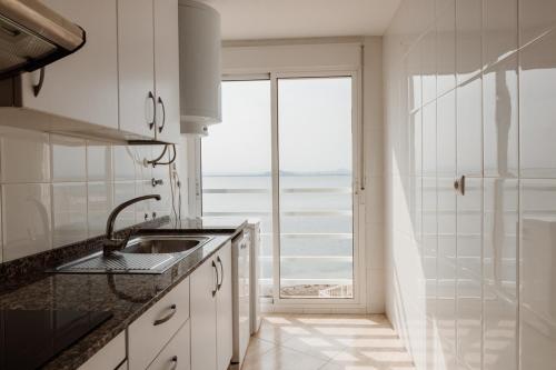 une cuisine blanche avec un évier et une grande fenêtre dans l'établissement Apartamentos Vistamar, à La Manga del Mar Meno