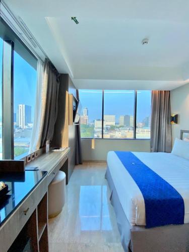 a hotel room with a bed and a desk and windows at Arthama Tanah Abang Jakarta in Jakarta