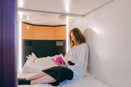 a woman sitting on a bed reading a book at NADESHIKO HOTEL TOKYO Shibuya by unito Female-only in Tokyo