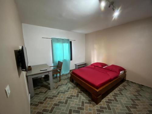 - une chambre avec un lit rouge, un bureau et une télévision dans l'établissement Résidences Gamly, à Mamoudzou