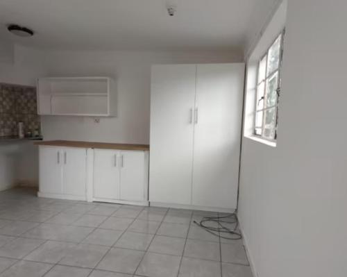 an empty kitchen with white cabinets and a window at Secret Sanctuary: Corner Cottage in Pietermaritzburg