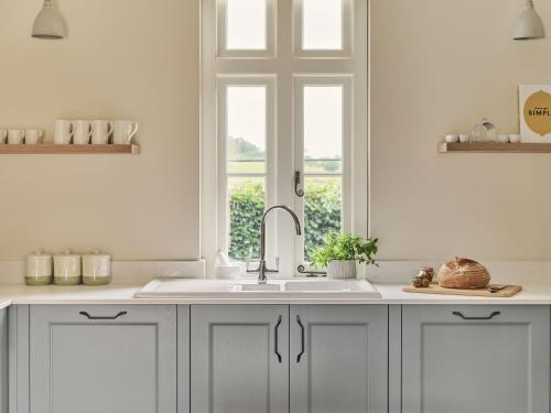 biała kuchnia ze zlewem i oknem w obiekcie Bridge House at Woodhall Estate w mieście Hertford