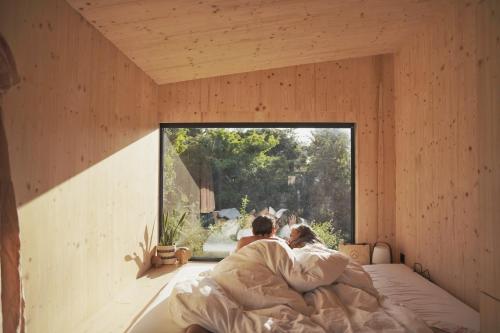 a couple laying in bed in a room with a window at Slow Cabins Kinvara in Kinvara