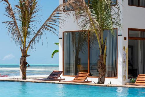 een zwembad met stoelen en palmbomen naast de oceaan bij S&S HOTEL in Jambiani