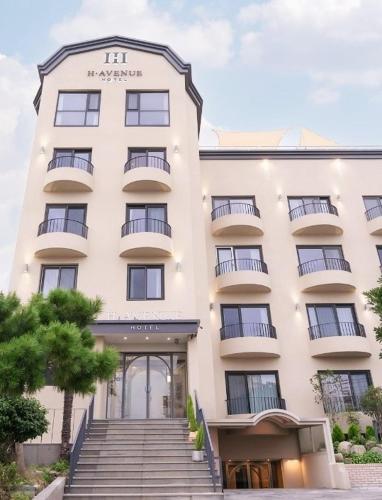 a large white building with stairs in front of it at Geoje Mongdol Beach H Avenue Hotel in Geoje 