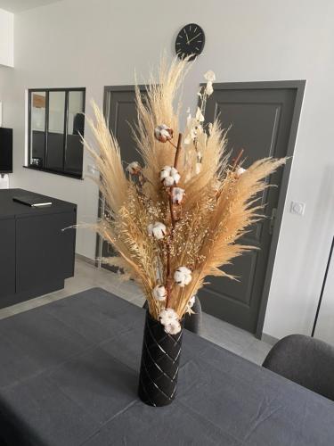 a black vase with grass and white flowers on a table at Le Merrain gîte plein coeur de Chablis in Chablis