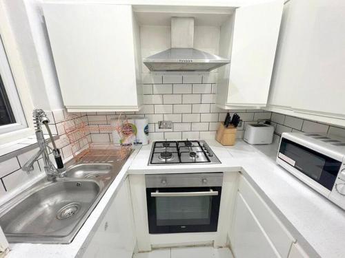 una cucina bianca con lavandino e piano cottura di 2-bedroom Apartment in Tooting a Londra