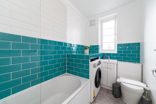 uma casa de banho com banheira, WC e azulejos azuis em The Crystal Palace Collection em Londres