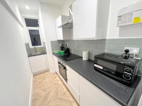 a kitchen with white cabinets and a black counter top at Ground Flr 3-bed flat near Norbury Station in Norbury