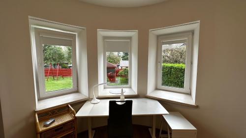 an office with three windows and a desk with a lamp at Japandi apartamentai in Kaunas