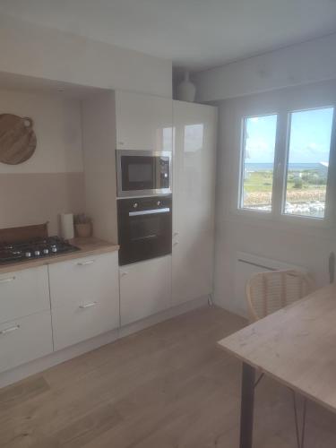uma cozinha com armários brancos, um micro-ondas e uma mesa em Appartement liberty em Courseulles-sur-Mer