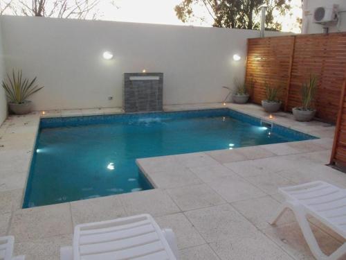 una piscina con 2 sillas blancas junto a una pared en Apart a metros de la laguna en Chascomús