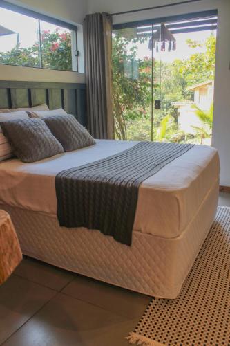 a large bed in a bedroom with a large window at Studio Bougainville - Praia do Rosa in Imbituba